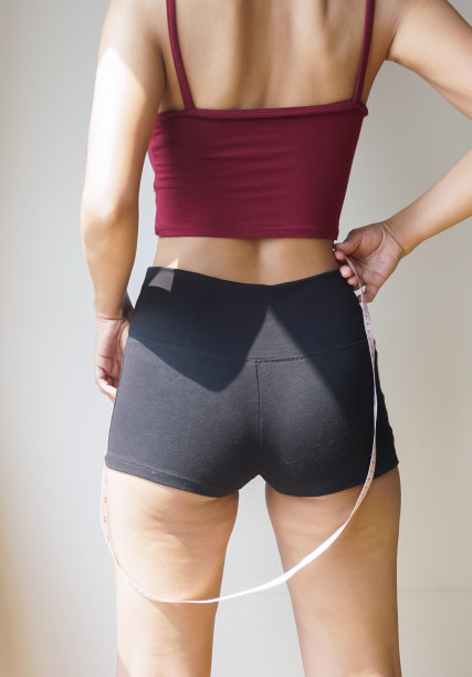 穿着红色衬衫和黑色短裤的瘦女人，站在后面，看到了腿上的脂肪团。图片下载