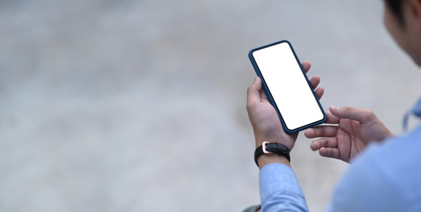 剪短的照片，年轻男子在蓝色衬衫拿着手机。空白屏幕用于图形显示蒙太奇。图片下载