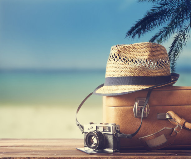 老式行李箱，时髦的帽子，相机和护照放在木架上。热带海洋，海滩和棕榈三的背景。图片下载