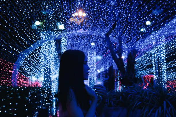 年轻美丽的女人喜欢参观缤纷的灯隧道在2021年新年节日和交通公园岛附近的钟塔图片下载