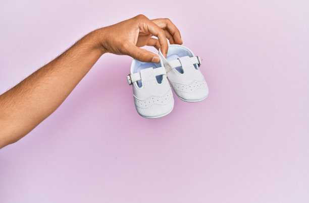 西班牙手抱婴儿鞋在孤立的粉红色背景。图片下载