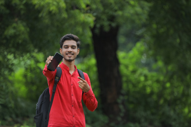 年轻的印度大学生在自然背景下展示智能手机图片下载