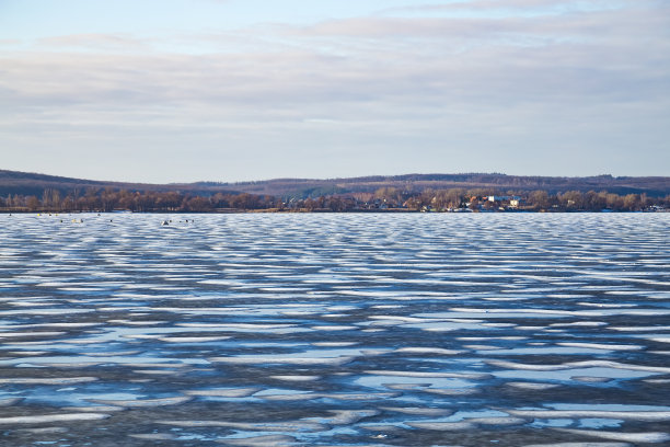 冬季景观冰冻湖在阳光明媚的日子。雪、冰和水坑。冬天在易碎的冰上行走是危险的。图片下载