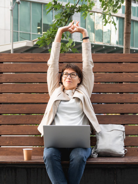 自由职业商务女性坐在公园里，手提电脑和带走纸杯咖啡。休闲服饰，千禧一代的都市生活方式。远程工作。图片下载