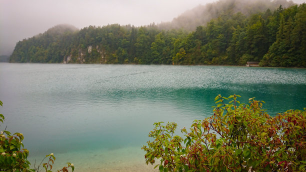 透过山中湖泊的灌木丛一瞥。背景中，群山笼罩在浓雾之中图片下载
