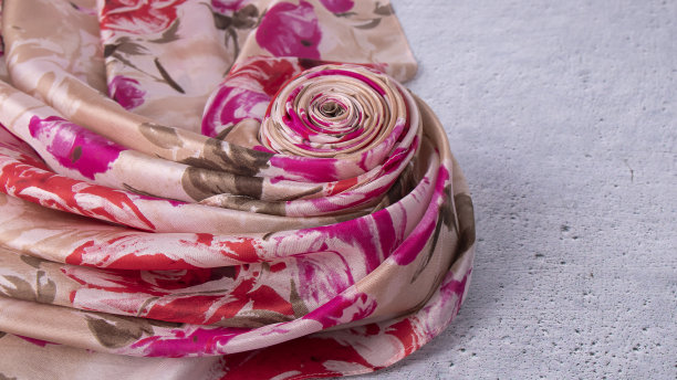 奢华的粉红色和红色的花图案丝巾漂亮地折叠在自然浅灰色的抹布表面。图片下载