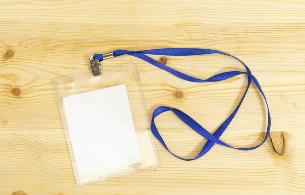 空白徽章模型孤立在木桌上。简单的空名字标签模拟挂在脖子上用绳子。姓名标签，企业设计。图片下载