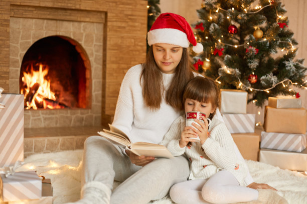 妈妈和她的女儿们坐在地板上柔软的地毯上看书，女孩子拿着杯子喝茶，妈妈拿着童话书，一起度过平安夜。图片下载