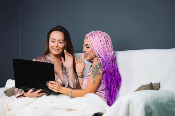 两个时尚的女朋友坐在家里，盖着被子，通过视频交流。住在一起的追随者图片下载