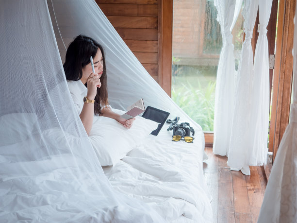 年轻的亚洲女性自由职业者在笔记本电脑和平板电脑远程工作，而休息在度假的卧室在暑假。图片下载