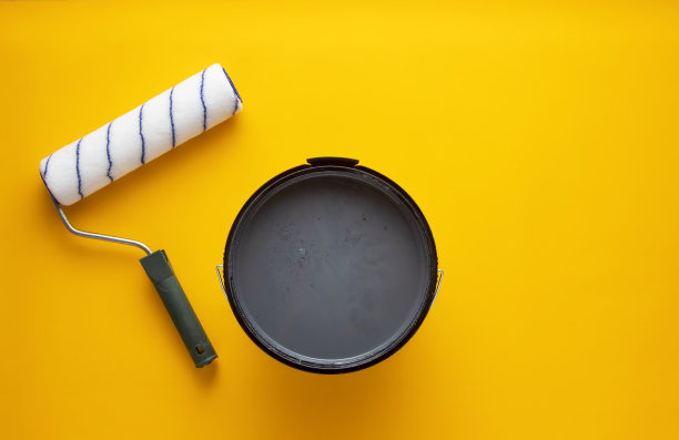 一罐灰色油漆与裤子辊在黄色的背景。素材图片