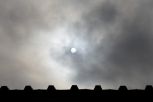 阴沉沉的天空上，白色的太阳和篱笆顶上的剪影。自然的灰蓝色背景图片下载