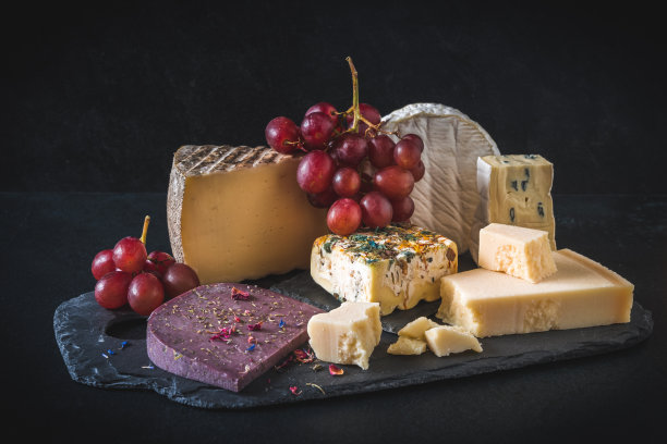 各种独特多彩的奶酪，以红葡萄装饰，黑色背景图片下载