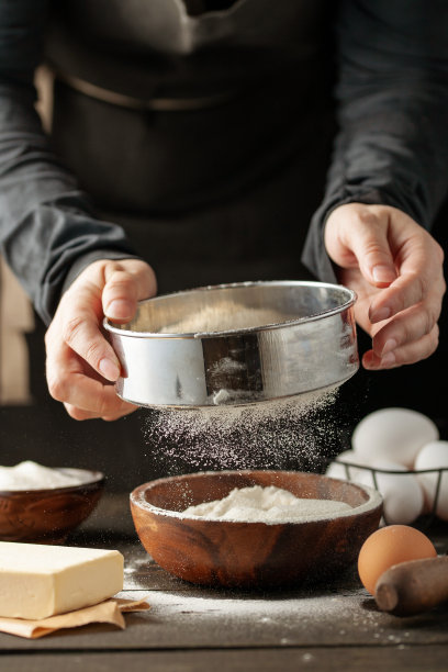 厨师用手将面粉粉倒入生面团上，用筛子在黑色的背景上，烹饪过程。图片下载