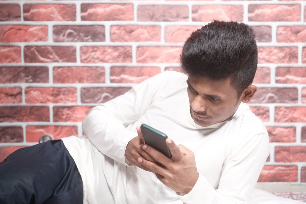 年轻人躺在床上玩智能手机。图片下载