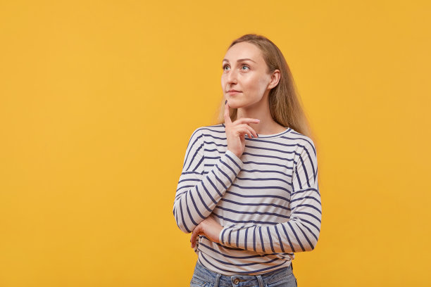 美丽的金发女人一边想一边看。黄色背景。图片下载