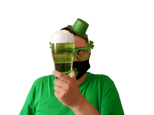 圣帕特里克节。一个年轻人穿着节日的服装，戴着帽子和眼镜，透过一杯绿色啤酒看出去图片下载