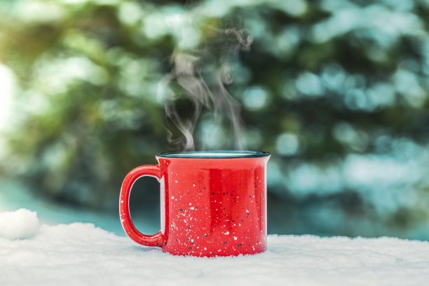 红色的杯子里放着冬天的热饮(热葡萄酒、可可、咖啡、茶)，背景是冬天的森林和积雪。冬天心情舒畅。图片下载