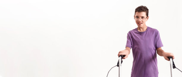 一个戴着眼镜的患有脑瘫的十几岁残疾男孩对着镜头微笑，在白色的背景下和他的步行者一起行走图片下载