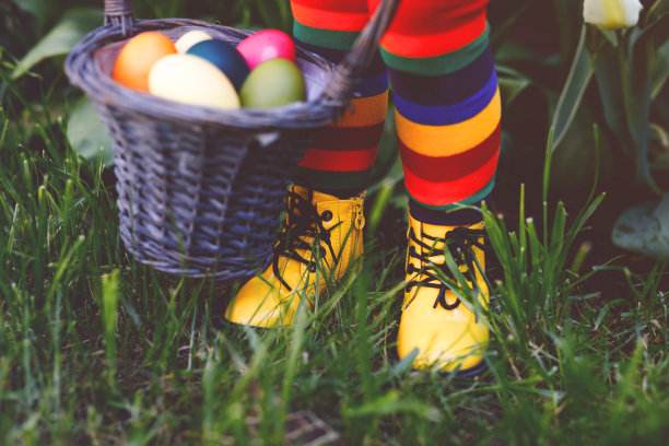 小女孩的腿的特写与彩色的袜子和鞋子和篮子与彩色的鸡蛋。孩子们在户外寻找传统的复活节彩蛋。庆祝基督教节日。图片下载