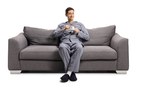 一个年轻人穿着睡衣坐在沙发上，手里拿着一杯浓咖啡图片下载