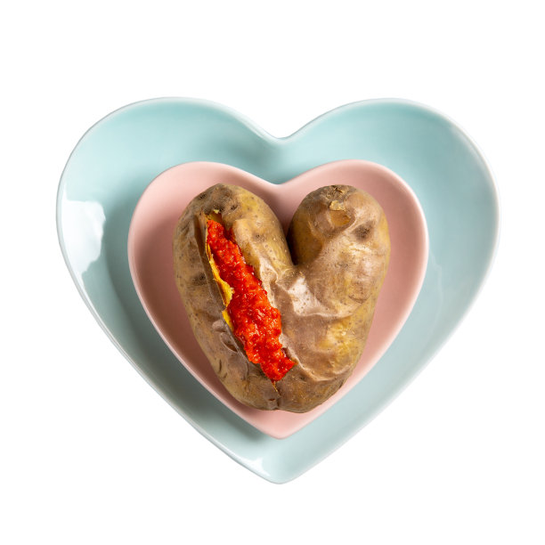 心形的土豆。配红酱的烤土豆放在心形的盘子里，白色的背景上。素食、素食的概念。前视图。图片下载