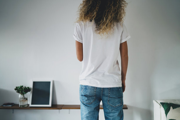 年轻的潮女穿着蓝色牛仔裤和空白的白色t恤，空白的标志，文字或设计。t恤的模型，白色的墙在背景。后视图。图片下载