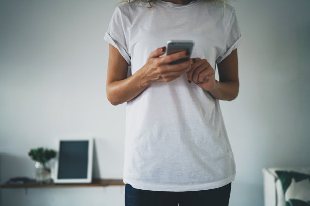 这是一张裁剪后的照片，照片上是一个穿着白色空白t恤和蓝色牛仔裤的苗条女孩。女性自由职业者使用手机进行远程工作。水平模拟，空设计位置图片下载