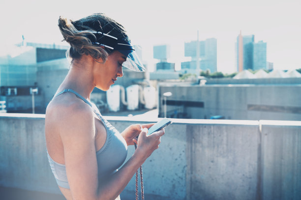 一个美丽的白人女性的侧视图照片检查早上锻炼训练的结果在手机应用程序。女运动员在晚上户外训练后回复信息。图片下载