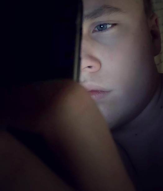 一个十几岁的男孩在黑暗中使用手机。图片下载