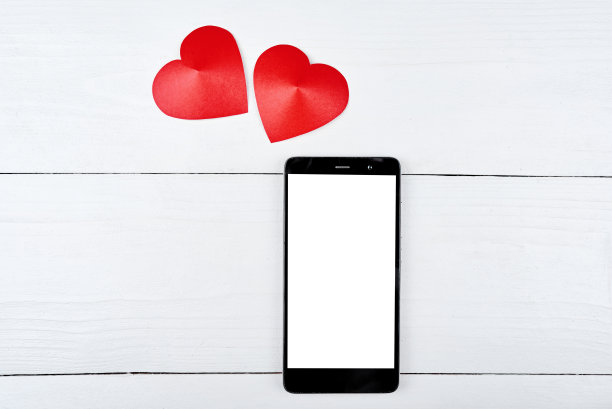 俯视图的移动智能手机与白色空白屏幕和两个红色纸心木制背景，复制空间。平躺，俯视图。情人节应用程序模型模板图片下载