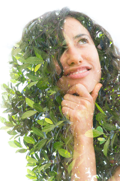 一张半微笑的沉思的年轻女子的双重曝光照片，卷曲的头发托着她的下巴和绿色的树叶图片下载