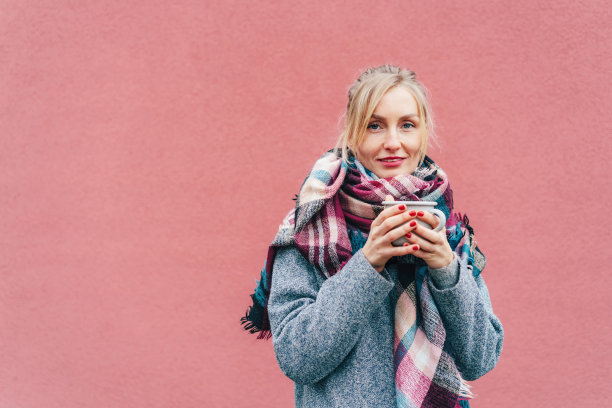 穿着大衣围着围巾的女人在冬天拿着杯子喝着饮料。图片下载
