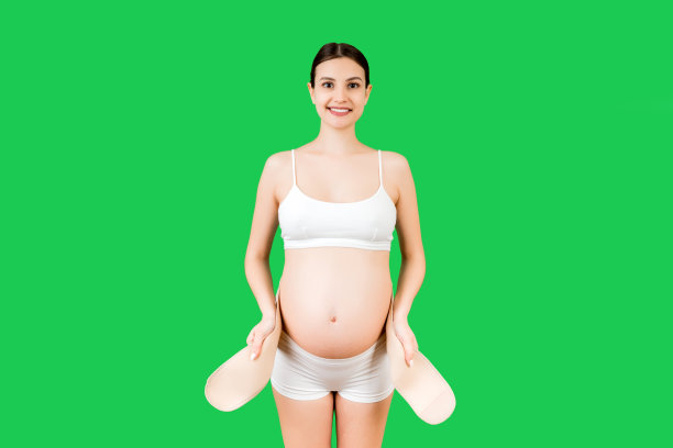 孕妇的肖像在内衣穿着孕妇带对疼痛在背后的绿色背景与复制空间。骨科腹部支撑带概念图片下载