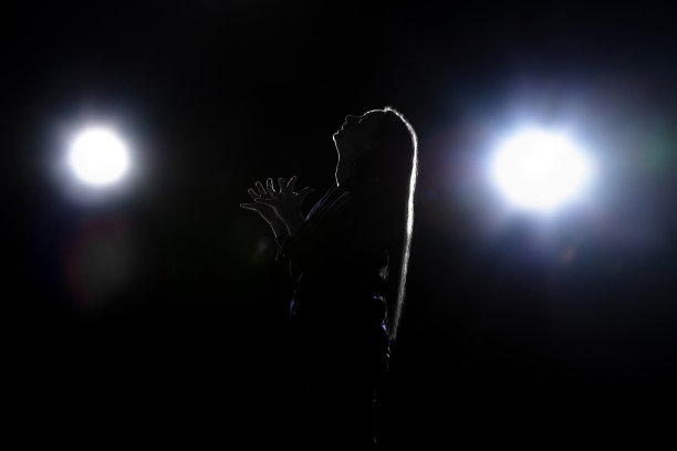 在灯笼的灯光下，在黑暗的背景上孤立祈祷的女人的剪影图片下载