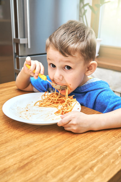 可爱的大眼睛的孩子吃着松软可口的意大利面图片下载