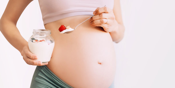 怀孕期间的营养和健康。特写孕妇的肚子与健康的零食酸奶，格兰诺拉麦片和浆果。图片下载