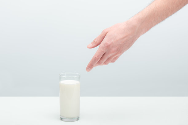 一个年轻人裸露的多毛的手伸向放在桌子上的一杯牛奶图片下载
