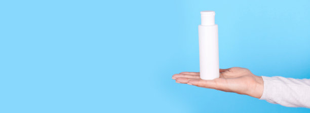 手拿白色洗液瓶放在蓝色底色上。图片下载