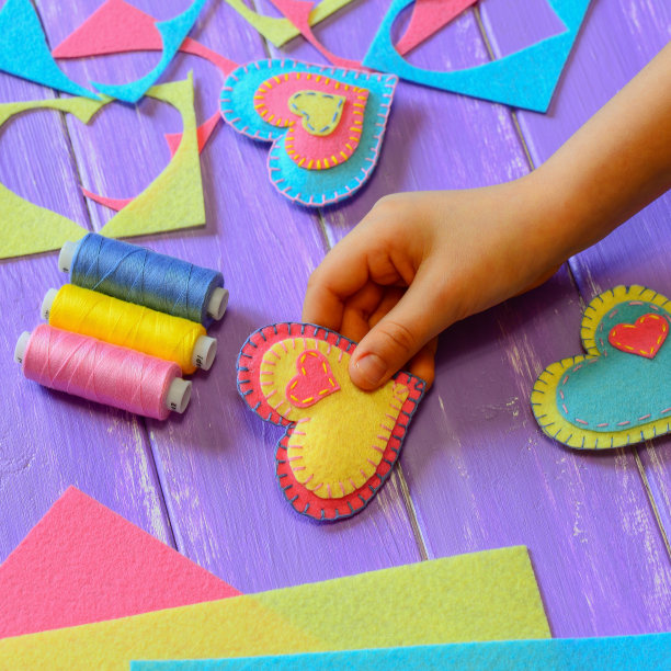 孩子表现出一种感觉爱的心装饰。这孩子为情人节做了一份贴心的礼物。明亮的毛毡心，线套，毛毡床单和碎片放在一张木桌上。小孩子学做针线活。简单的缝纫的爱好。简单的缝纫的爱好。缝纫项目图片下载