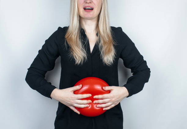 胀气和胀气的概念。女人在腹部附近拿着一个红色的气球，象征着腹胀。肠道和消化系统。肠胃气胀和胃肠道问题图片下载