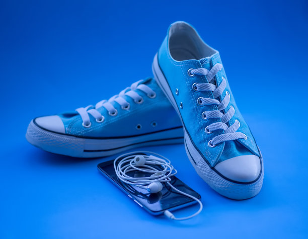 蓝色背景下的蓝色运动鞋，手机和耳机。青年的鞋子。运动和音乐的概念。图片下载