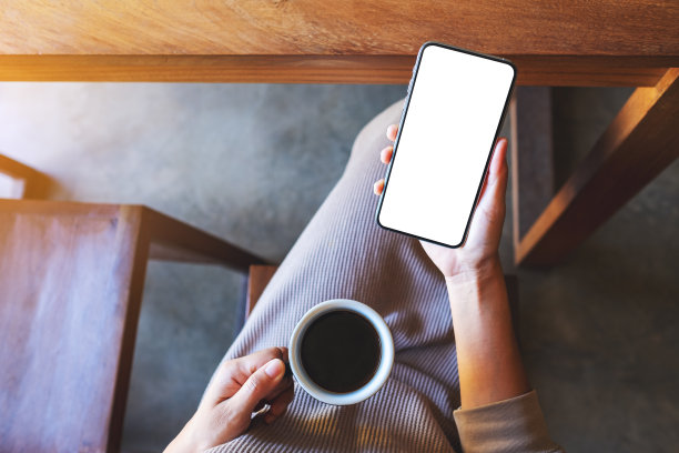 一个女人拿着手机和空白的桌面屏幕喝咖啡图片下载
