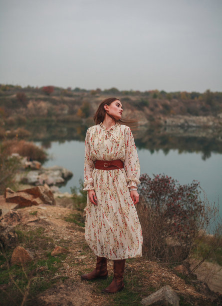 穿着长裙和棕色靴子的时尚模特在乡村的湖边摆姿势图片下载