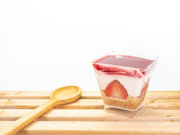 草莓芝士蛋糕装在透明的方形塑料杯里，放在木板上图片下载