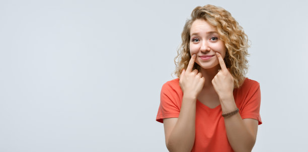 年轻漂亮的女人假装微笑，她的嘴伸展成微笑。假笑的概念。本空间图片下载