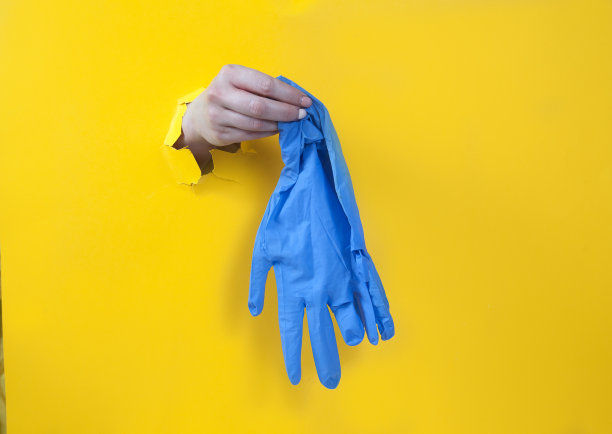女人的手拿着黄色背景上的蓝色橡胶手套。把手放在洞里。卫生。纯洁。covtd-19图片下载