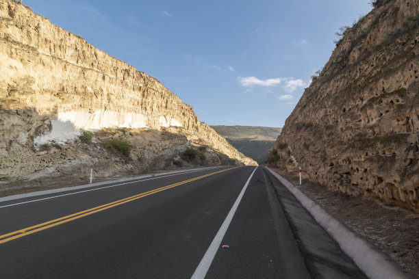 在一个阳光明媚的日子里，有岩石墙壁的道路景观和晴朗的天空，旅行和生活方式图片下载