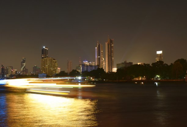 夜晚，模糊的船只在河流附近的建筑背景中移动图片下载