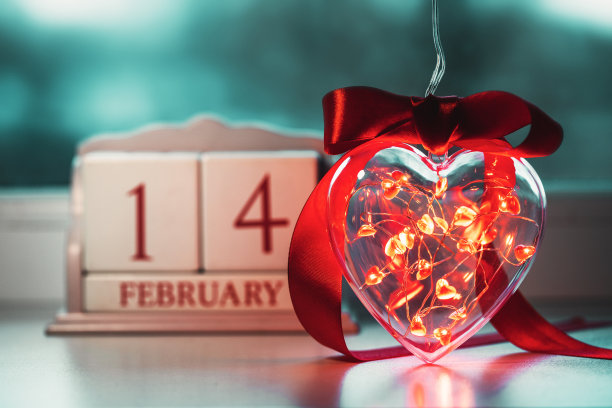 透明的塑料心，里面装满了发光的金属花环，还有心形灯泡和2月14日的老式日历。情人节的概念。图片下载